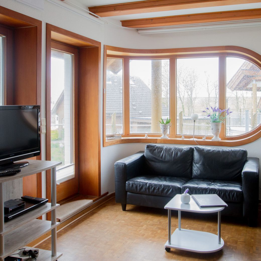 Wohungbereich mit TV und Couch, Panoramafenster & Balkonzugang