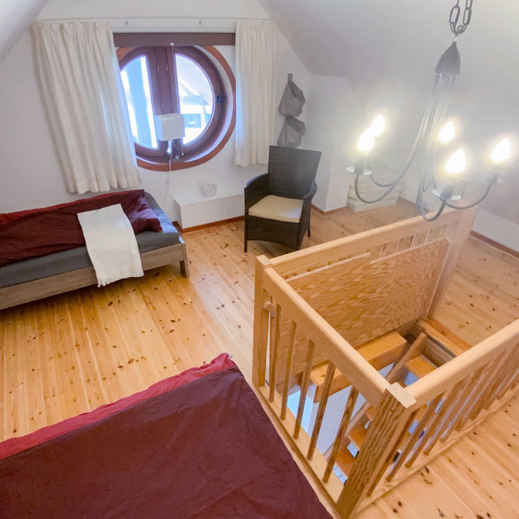 Schlafbereich im Dachgeschoss mit zwei Einzelbetten & rundem Fenster und Stuhl