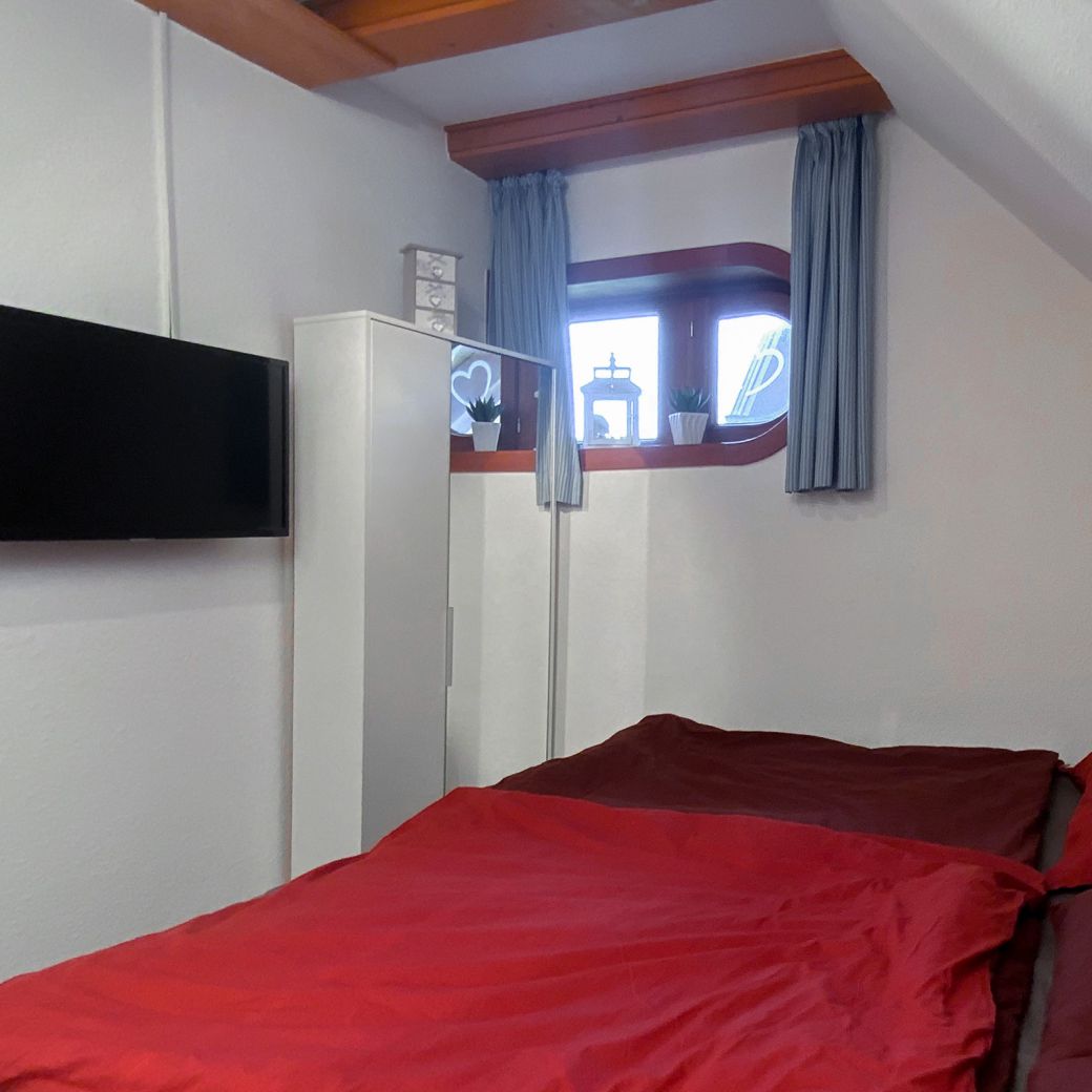 andere Perspektive ins Schlafzimmer mit Doppelbett, TV, Kleiderschrank und Fenster