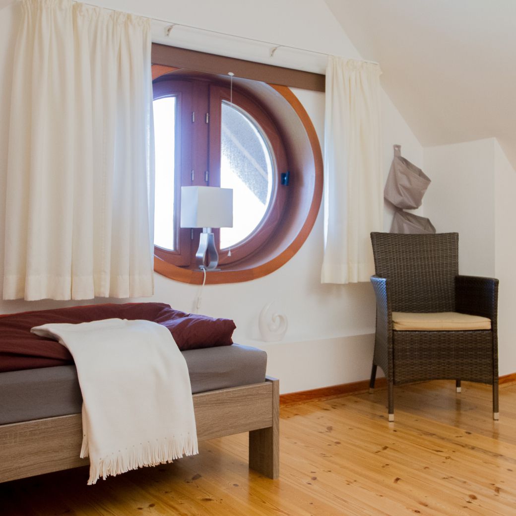 Schlafbereich im Dachgeschoss mit Einzelbett & rundem Fenster und Stuhl